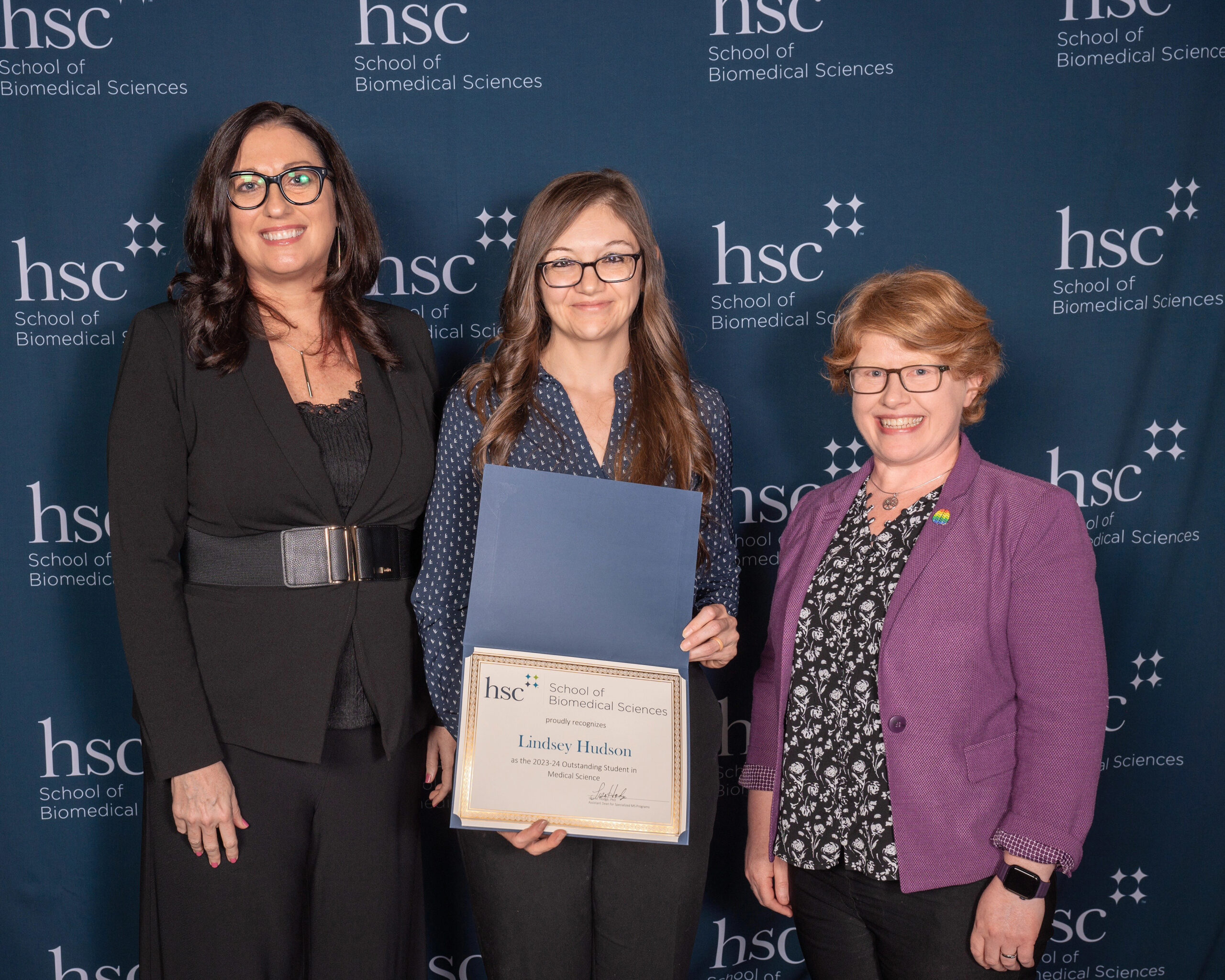 HSC School of Biomedical Science awards with Lindsey Hudson standing between two SBS faculty with her award