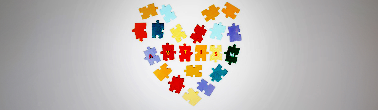 Photo of colorful puzzle pieces placed in shape of a heart with the word AUTISM spelled out on the middle row of pieces