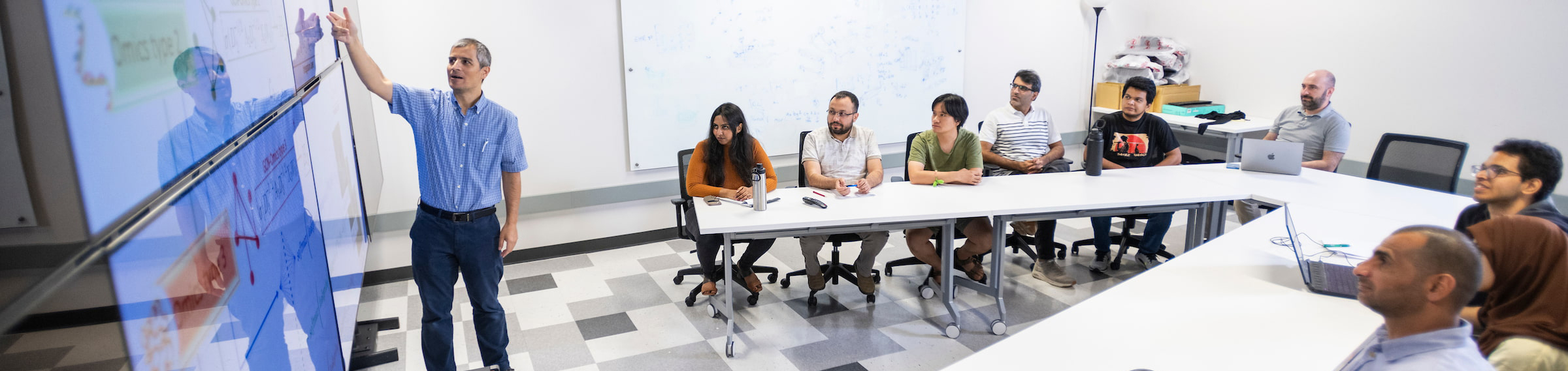 UNT's Dr. Serdar Bozdag explaining formulae on a board to a group of students