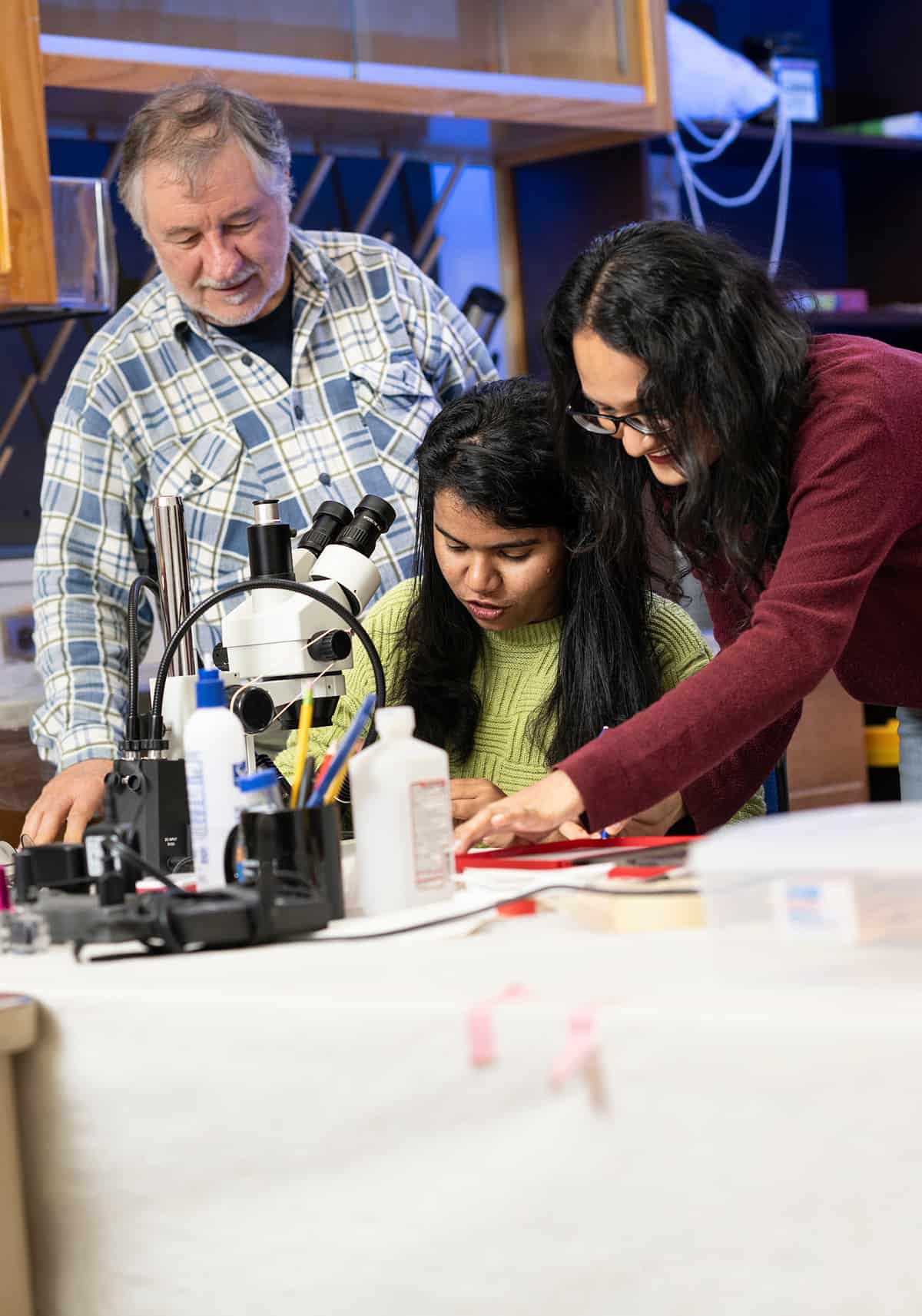 Photo of UNT's Dr. Jiménez with two UNT student researchers study moss and lichen samples under a microscope Photo of three UNT researchers study moss and lichen samples under a microscope